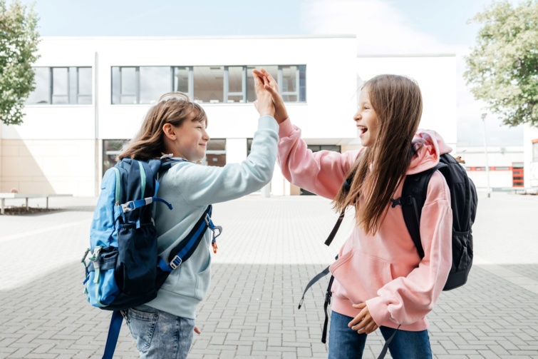 Két diáklány üdvözli egymást az iskola előtt.